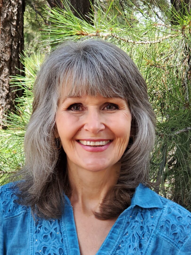 A woman with grey hair and blue shirt smiling.